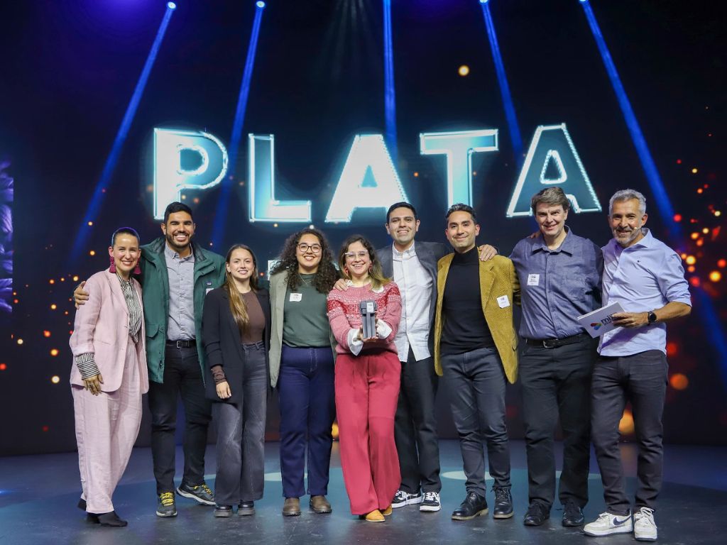 Equipos de Modista y Cebra celebrando en el escenario junto al letrero “Plata” de los IAB MIXX Chile 2026, con el trofeo en las manos.